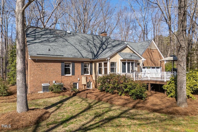 rear view of house with brick siding, cooling unit, a chimney, a deck, and a yard