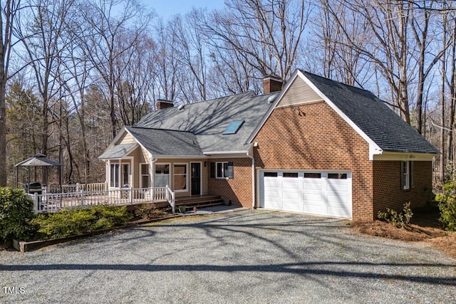 view of front facade featuring brick siding, gravel driveway, covered porch, a chimney, and an attached garage