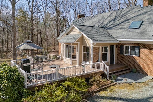 view of side of property featuring a gazebo, a shingled roof, a wooden deck, brick siding, and a chimney