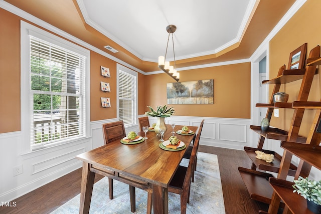 dining space featuring dark wood-style floors, crown molding, wainscoting, a tray ceiling, and a decorative wall