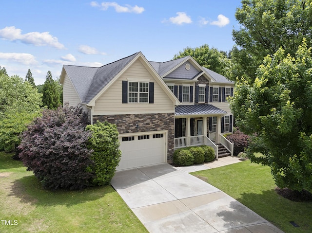 view of front facade with covered porch, stone siding, driveway, a front yard, and a garage