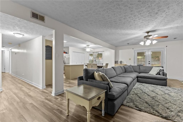 living room with light wood-style flooring, a ceiling fan, visible vents, and a textured ceiling