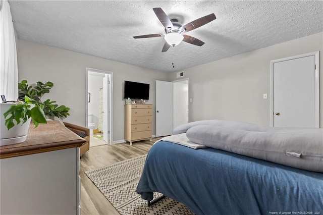 bedroom with light wood-type flooring, a textured ceiling, connected bathroom, and a ceiling fan