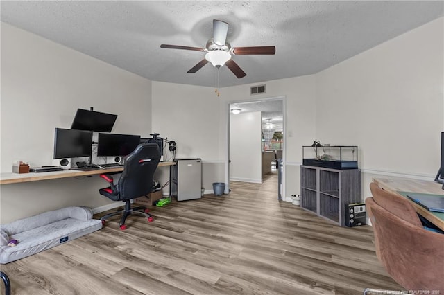 home office with visible vents, a textured ceiling, a ceiling fan, and wood finished floors