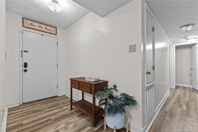entryway with visible vents, light wood-style flooring, a textured ceiling, and baseboards