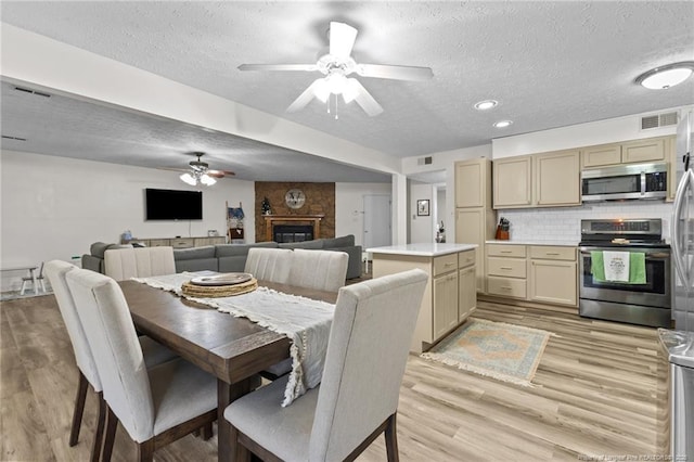 dining space with visible vents, light wood-type flooring, a fireplace, a textured ceiling, and a ceiling fan