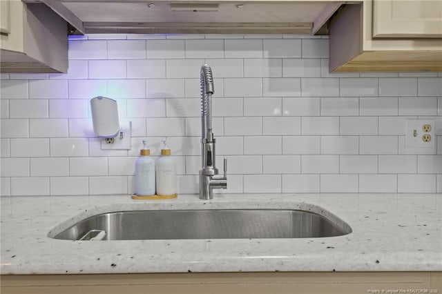 interior details with light stone counters, backsplash, and a sink