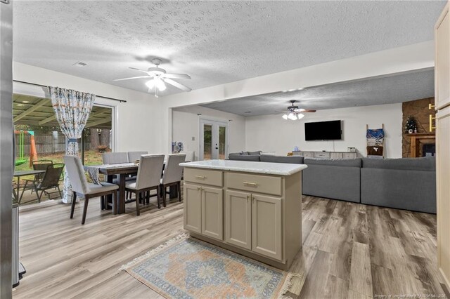 kitchen with light wood-type flooring, gray cabinetry, ceiling fan with notable chandelier, a textured ceiling, and a kitchen island