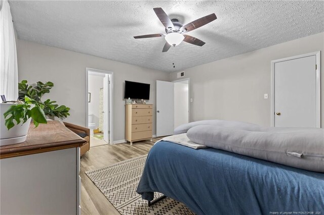 bedroom with visible vents, ceiling fan, light wood-type flooring, ensuite bathroom, and a textured ceiling