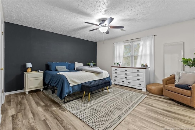 bedroom with light wood-type flooring, a ceiling fan, a textured ceiling, baseboards, and an accent wall