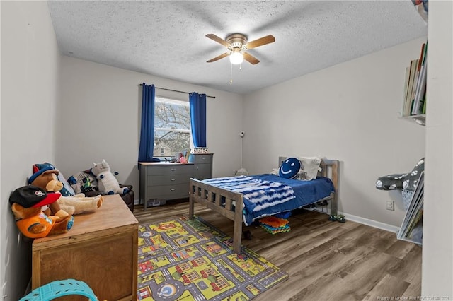 bedroom featuring light wood finished floors, ceiling fan, a textured ceiling, and baseboards