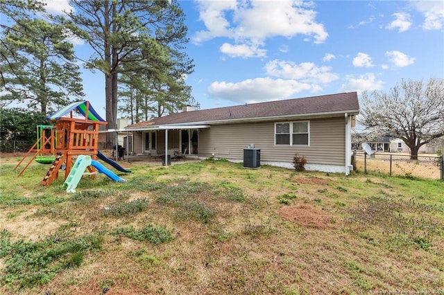 rear view of property with a yard, fence, central AC, and a playground