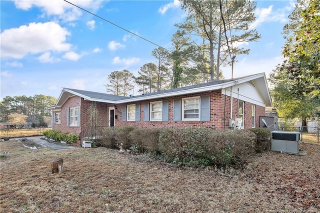 view of front of home featuring brick siding, central air condition unit, and fence