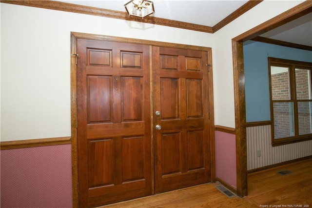 foyer entrance featuring visible vents, a wainscoted wall, wood finished floors, and crown molding