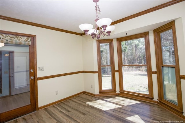 unfurnished dining area featuring a chandelier, baseboards, wood finished floors, and crown molding