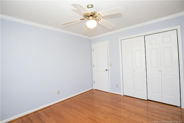 unfurnished bedroom with wood finished floors, a closet, crown molding, baseboards, and ceiling fan