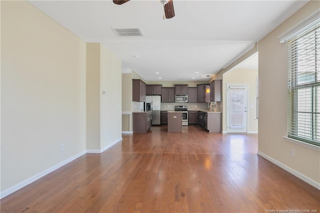 unfurnished living room featuring wood finished floors, a ceiling fan, visible vents, and baseboards