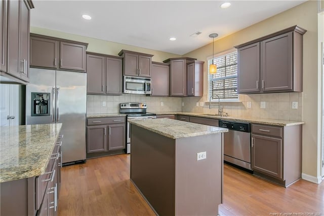 kitchen with a sink, a kitchen island, appliances with stainless steel finishes, and wood finished floors