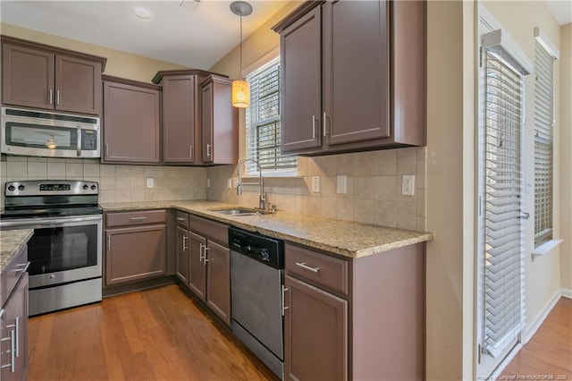 kitchen with a sink, light stone counters, wood finished floors, appliances with stainless steel finishes, and decorative backsplash