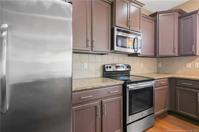 kitchen featuring backsplash, light stone countertops, light wood-type flooring, and appliances with stainless steel finishes