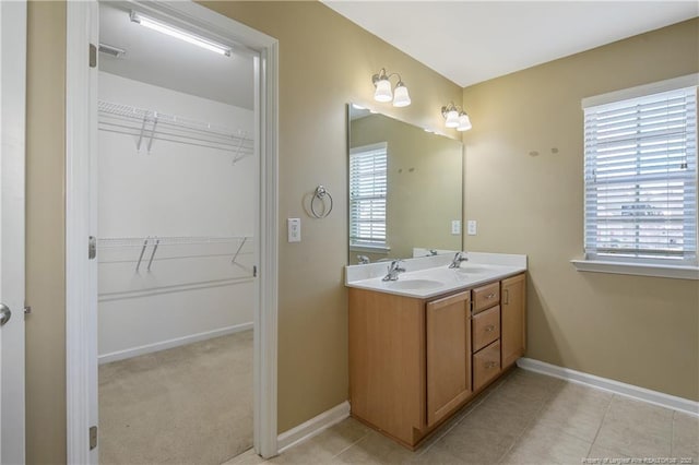 bathroom with a sink, a walk in closet, baseboards, and double vanity