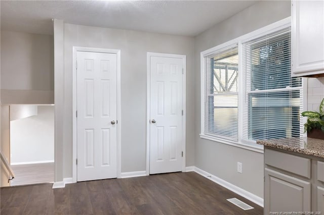 unfurnished bedroom with dark wood-style floors, visible vents, two closets, and baseboards