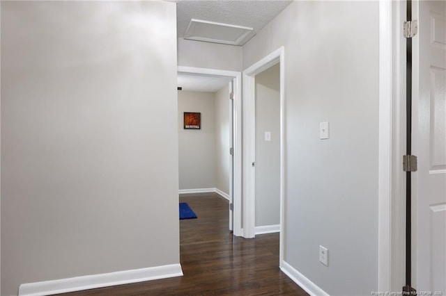 corridor with dark wood finished floors, attic access, baseboards, and a textured ceiling