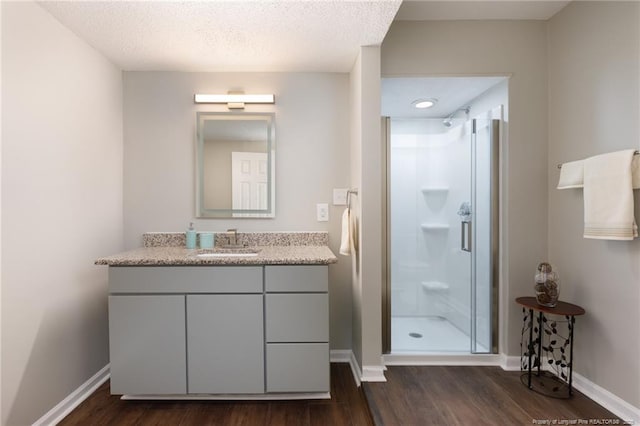 full bathroom with a shower stall, vanity, baseboards, and wood finished floors