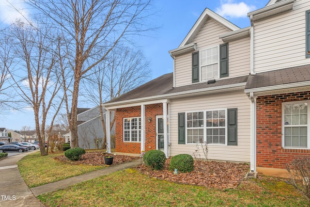 view of front of house featuring brick siding, a shingled roof, and a front yard