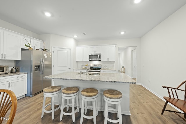 kitchen with light wood-type flooring, a sink, appliances with stainless steel finishes, white cabinetry, and tasteful backsplash