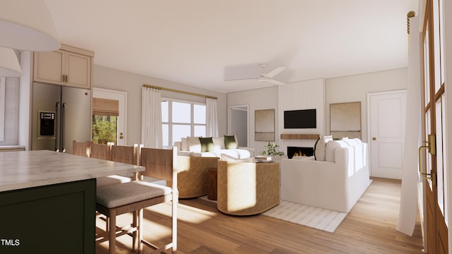 living room with light wood-style flooring, a warm lit fireplace, and ceiling fan