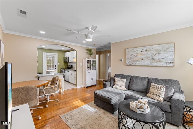 living room with visible vents, light wood finished floors, arched walkways, ceiling fan, and crown molding