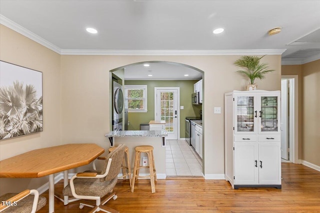 dining space featuring light wood finished floors, crown molding, baseboards, recessed lighting, and arched walkways