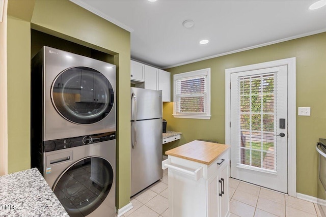 laundry area featuring laundry area, stacked washer and dryer, light tile patterned flooring, and crown molding