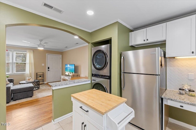 kitchen featuring visible vents, stacked washer and dryer, freestanding refrigerator, arched walkways, and white cabinets