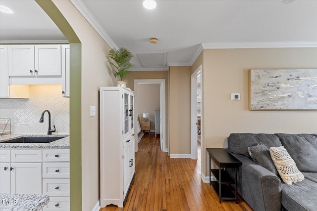 corridor with crown molding, baseboards, wood finished floors, arched walkways, and a sink