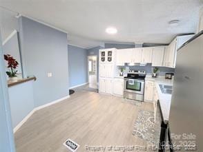 kitchen with light wood finished floors, electric range, white cabinets, and light countertops