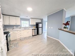 kitchen featuring a sink, light wood-style floors, appliances with stainless steel finishes, white cabinets, and light countertops