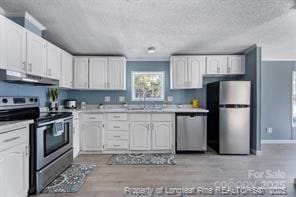 kitchen with under cabinet range hood, white cabinets, appliances with stainless steel finishes, and light countertops