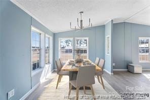 dining space with baseboards, lofted ceiling, wood finished floors, a notable chandelier, and a textured ceiling