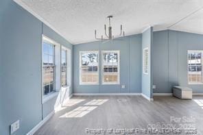 unfurnished dining area featuring a notable chandelier, a textured ceiling, wood finished floors, baseboards, and vaulted ceiling