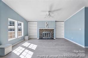 unfurnished living room featuring wood finished floors, baseboards, ceiling fan, a stone fireplace, and vaulted ceiling