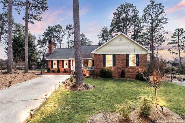 ranch-style home featuring brick siding, driveway, a chimney, and a front lawn