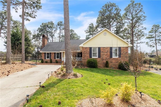 single story home with brick siding, a chimney, concrete driveway, and a front yard