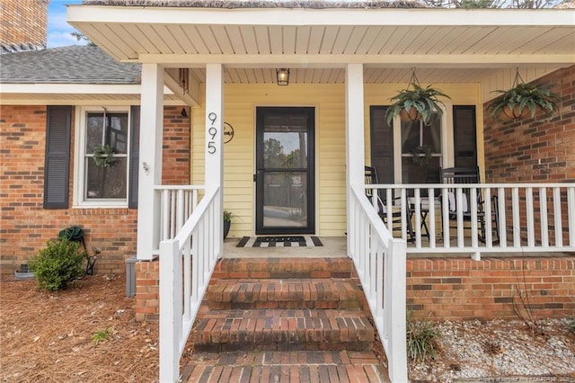 property entrance featuring a porch, brick siding, and a shingled roof