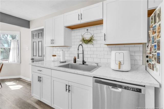 kitchen featuring tasteful backsplash, stainless steel dishwasher, wood finished floors, white cabinets, and a sink