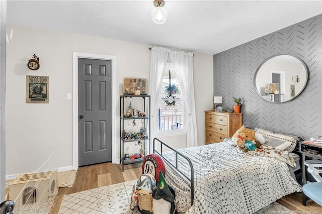 bedroom with visible vents, wallpapered walls, an accent wall, baseboards, and wood finished floors