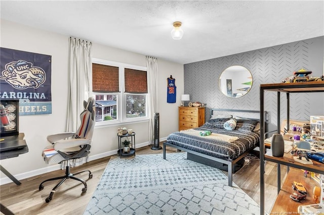 bedroom featuring wallpapered walls, baseboards, an accent wall, and light wood finished floors