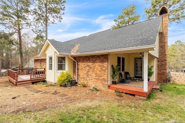 back of property featuring a wooden deck, brick siding, roof with shingles, and a chimney