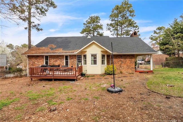 back of property featuring fence, a wooden deck, a chimney, a shingled roof, and brick siding